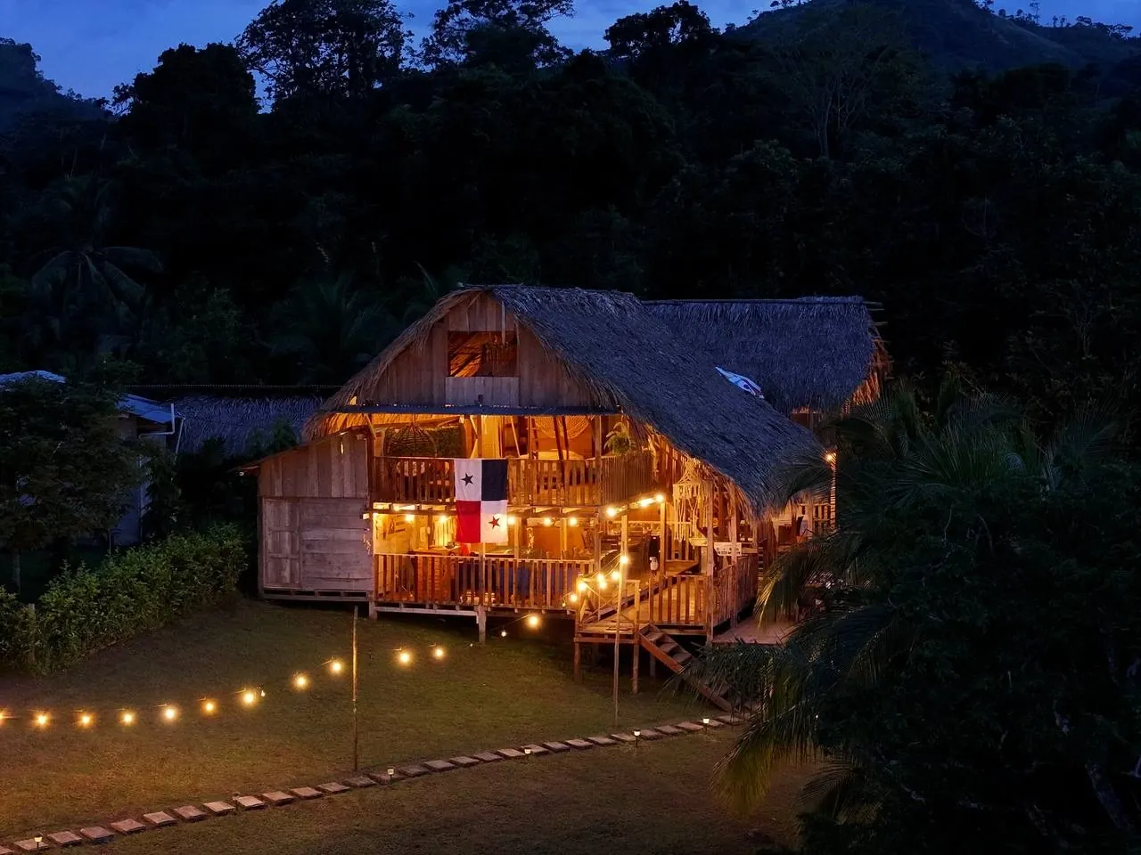 La cabaña de noche, con la bandera de Panamá en el balcón y el bosque de fondo.